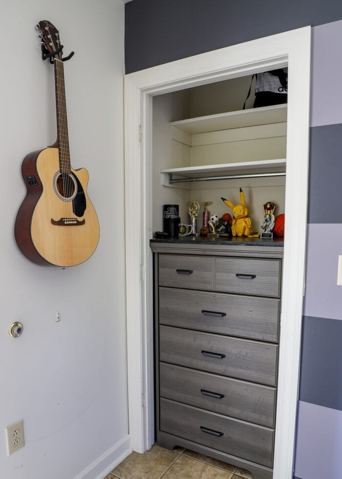 Guitar on the wall next to a dresser inside a closet in a small teen bedroom