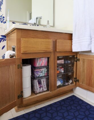 Oak cabinet under the bathroom sink organized with clear acrylic drawers to hold toiletries