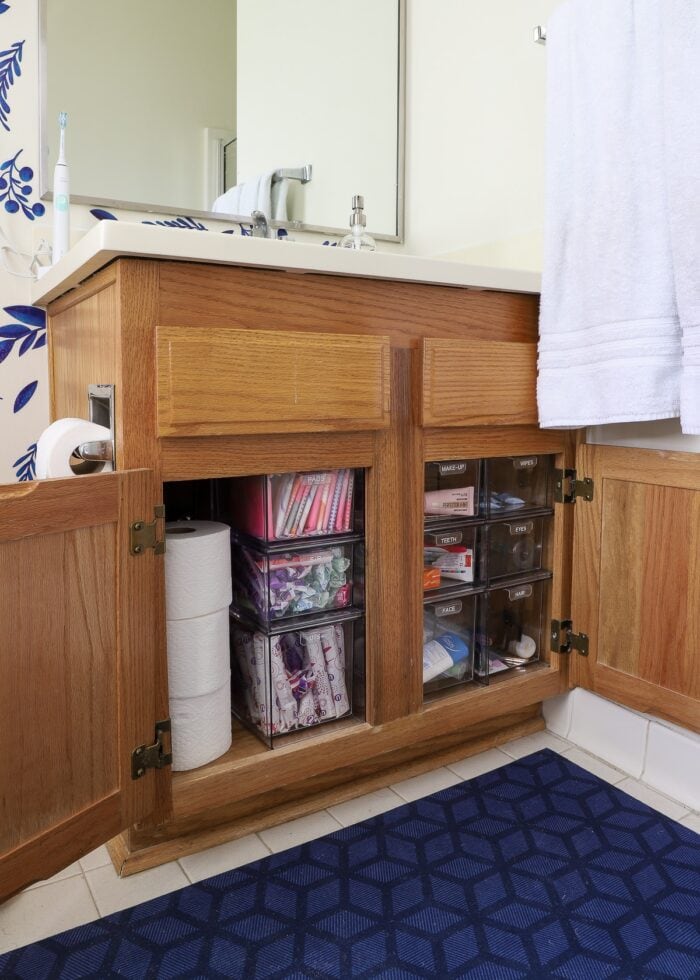 Oak cabinet under the bathroom sink organized with clear acrylic drawers to hold toiletries