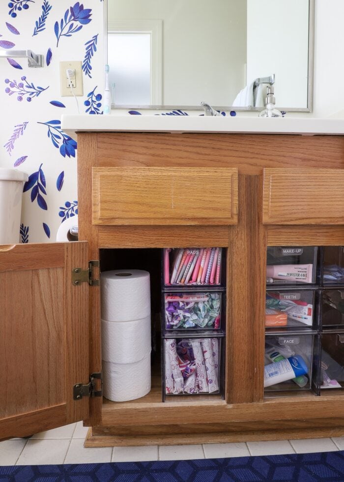 Oak cabinet under the bathroom sink organized with clear acrylic drawers to hold toiletries