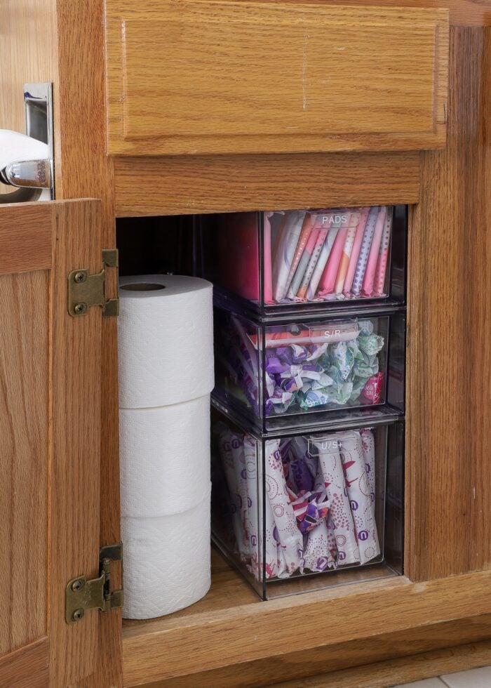 Clear acrylic drawers holding hygiene supplies under a bathroom sink