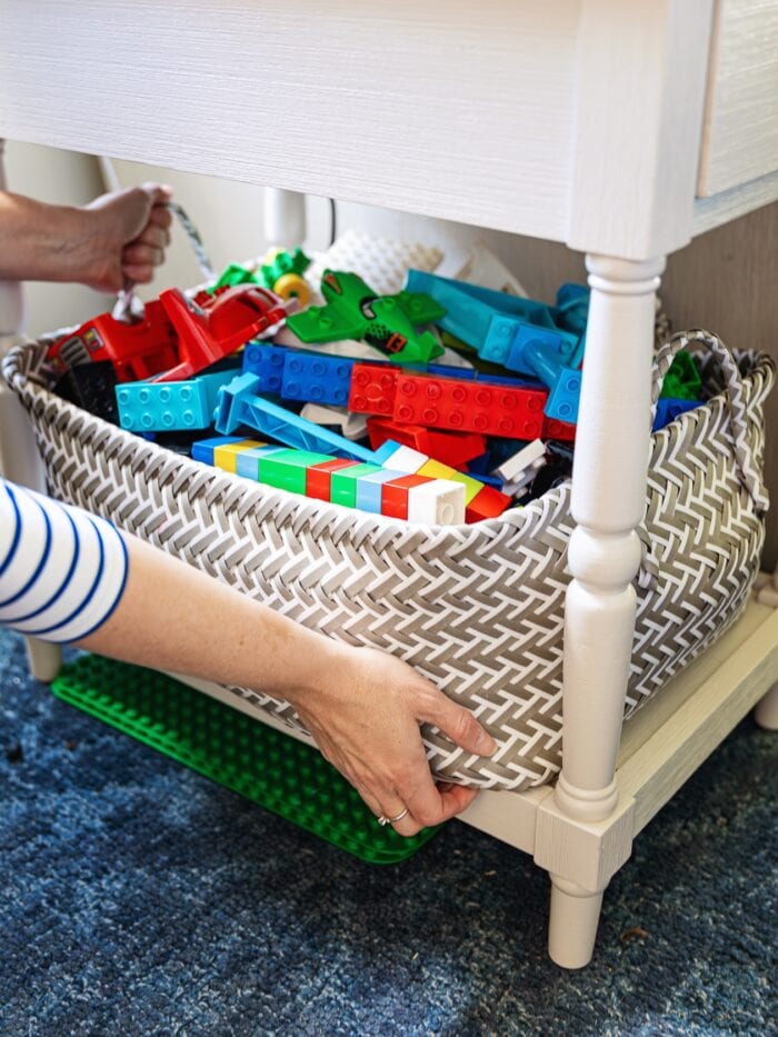 Hands placing a basket of Duplo blocks under a side table