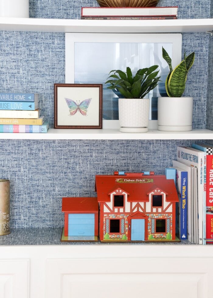 Fisher Price Dollhouse on a white bookcase with blue wallpaper alng the back