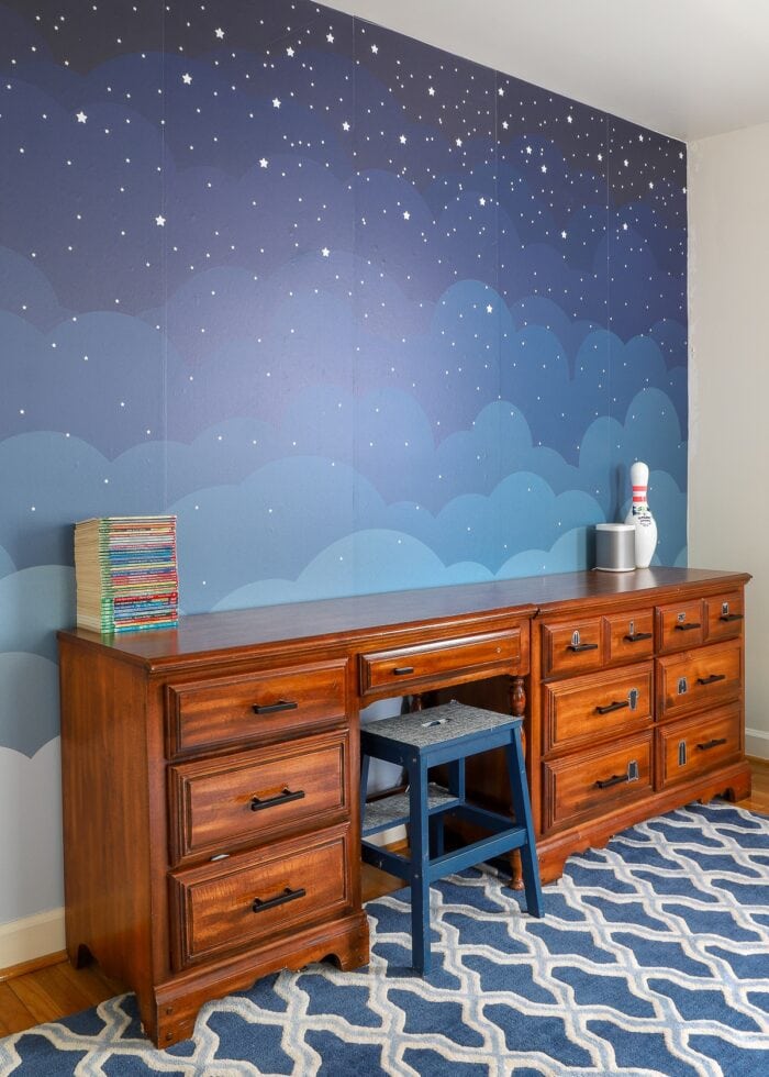 A wallpaper mural of the night sky on a boys' shared bedroom wall
