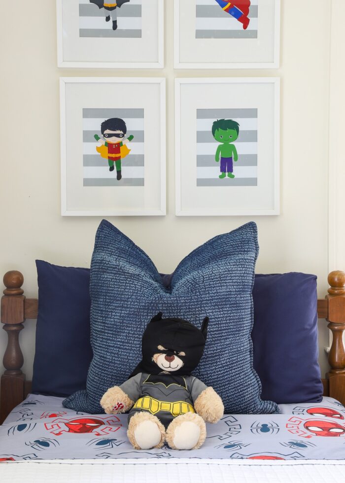 A boys' twin bed with super hero artwork and a Batman bear on the pillow