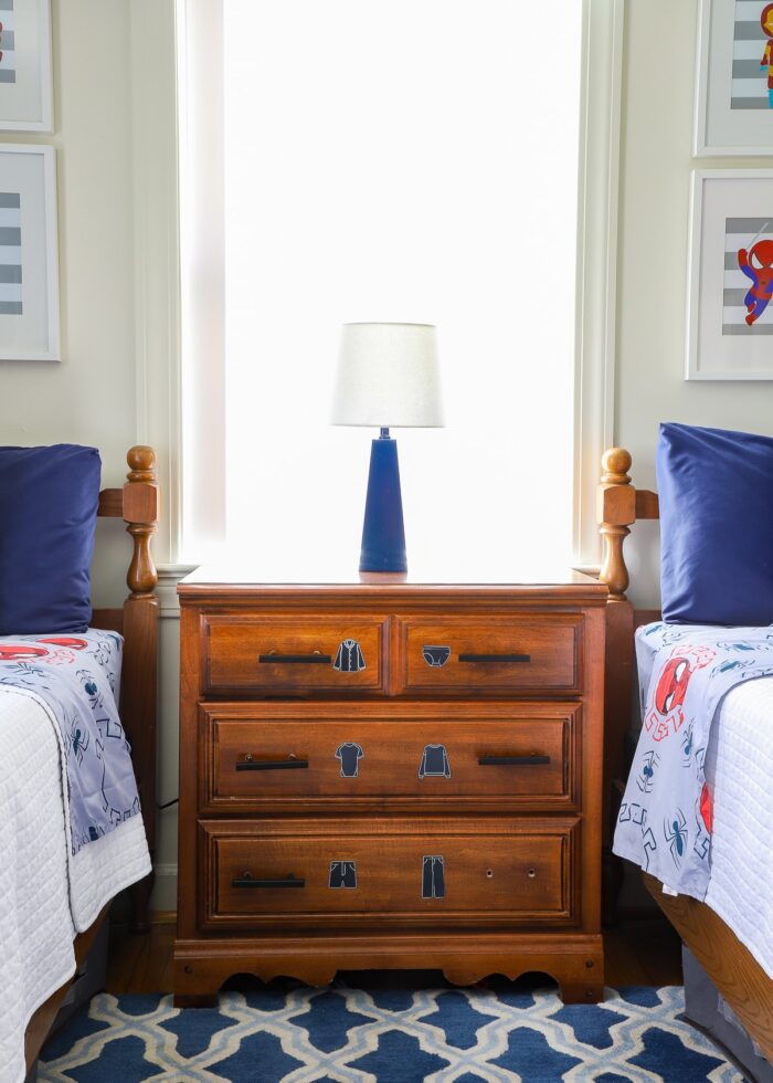 A small dresser in between two twin beds with a blue lamp on top