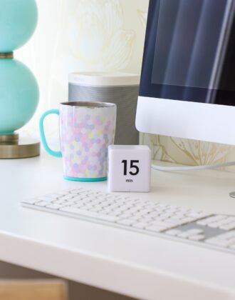 Coffee cup and timer on a white desk next to keyboard