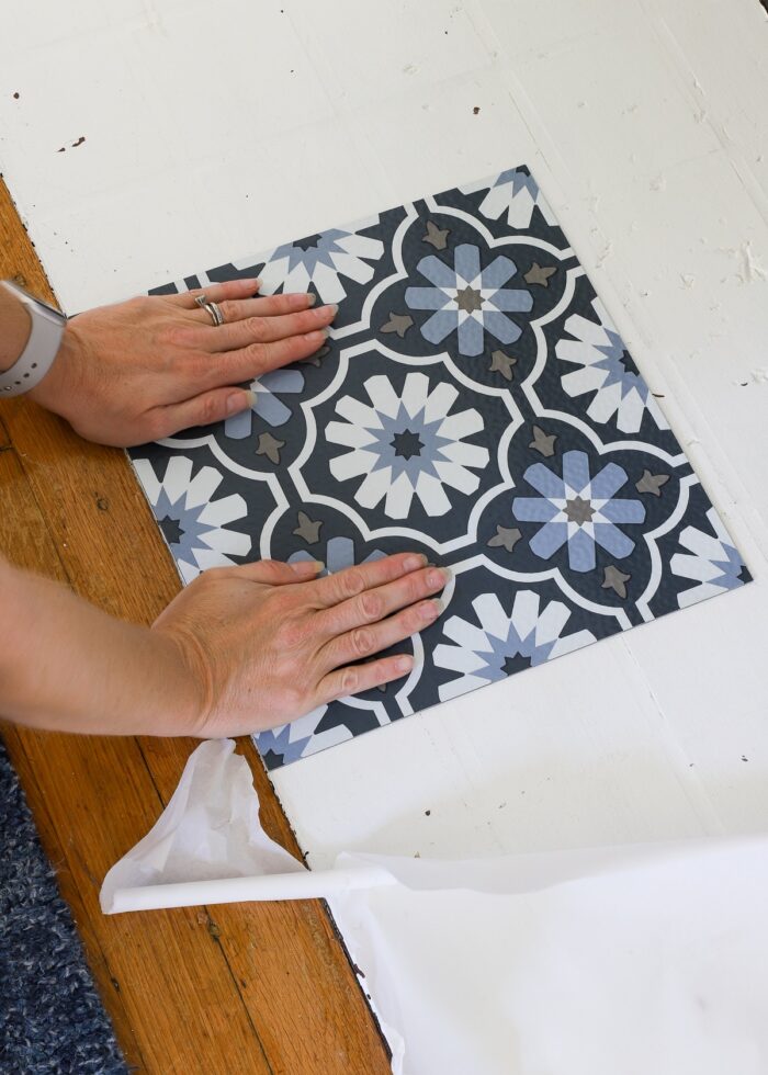 Hands sticking a Floor Pops! peel and stick floor tile onto a white fireplace hearth