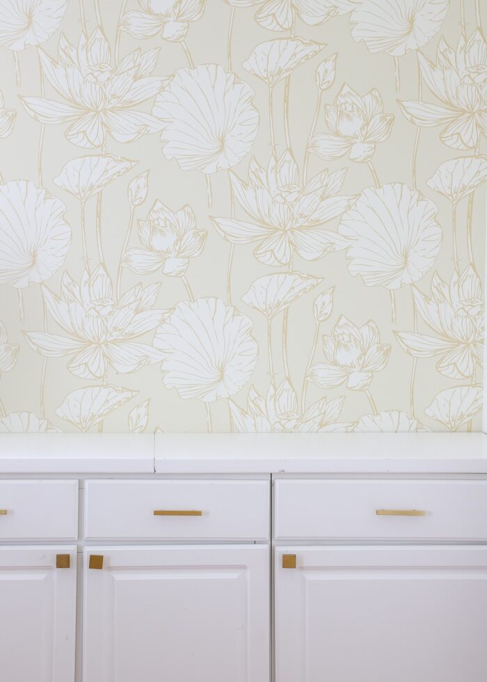 White lower cabinets and countertops against a wall with beige floral wallpaper above it