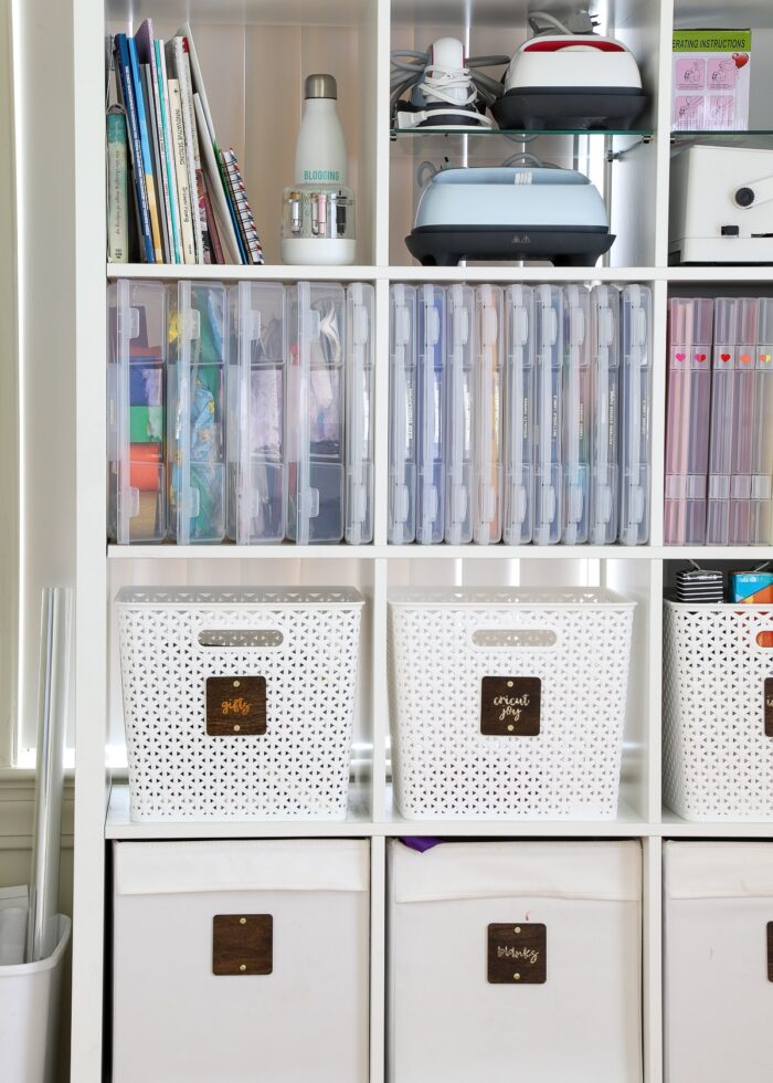 A variety of white baskets and clear storage cases holding craft supplies on a white shelf