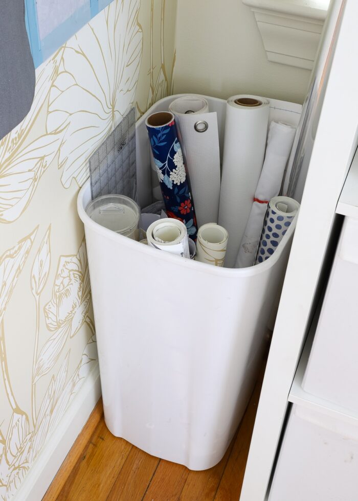 White trash can holding rolls of wallpaper and contact paper