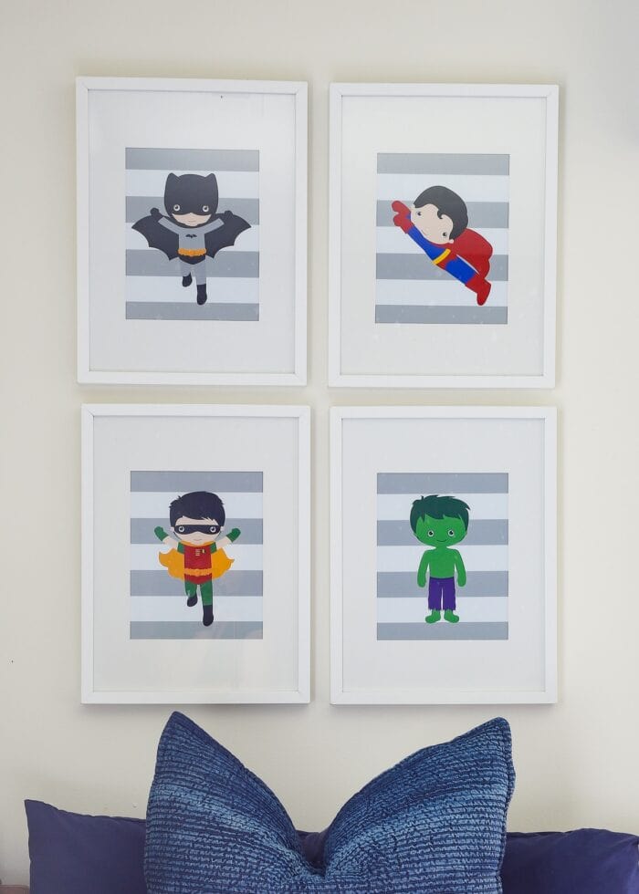 A collection of 4 mini super hero prints in white frames above a bed