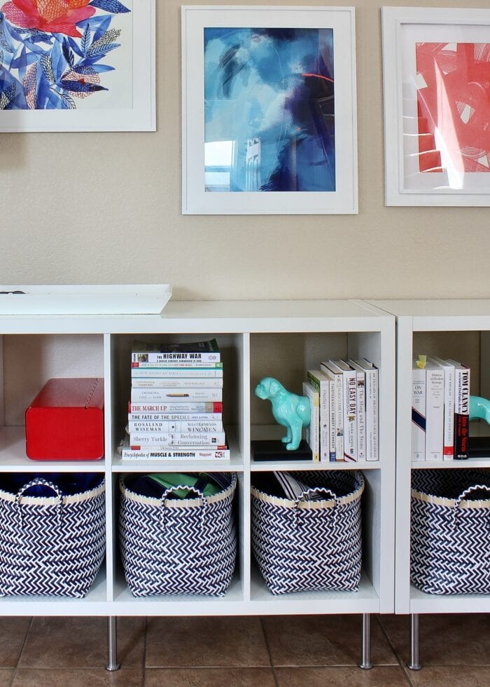 While Kallax bookshelves filled with white books, blue baskets, and colorful artwork hung above