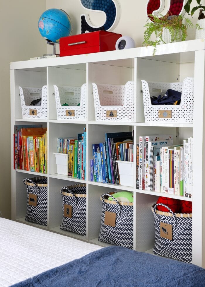 IKEA Kallax shelf holding books organized by color and accessorized with baskets