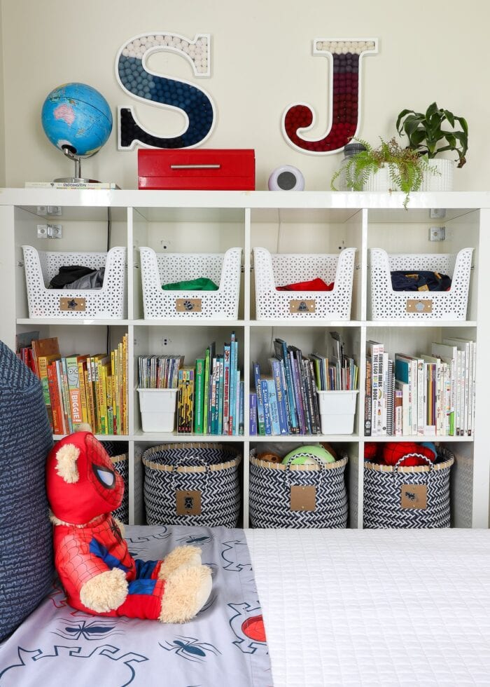 IKEA Kallax shelf holding books organized by color and accessorized with baskets