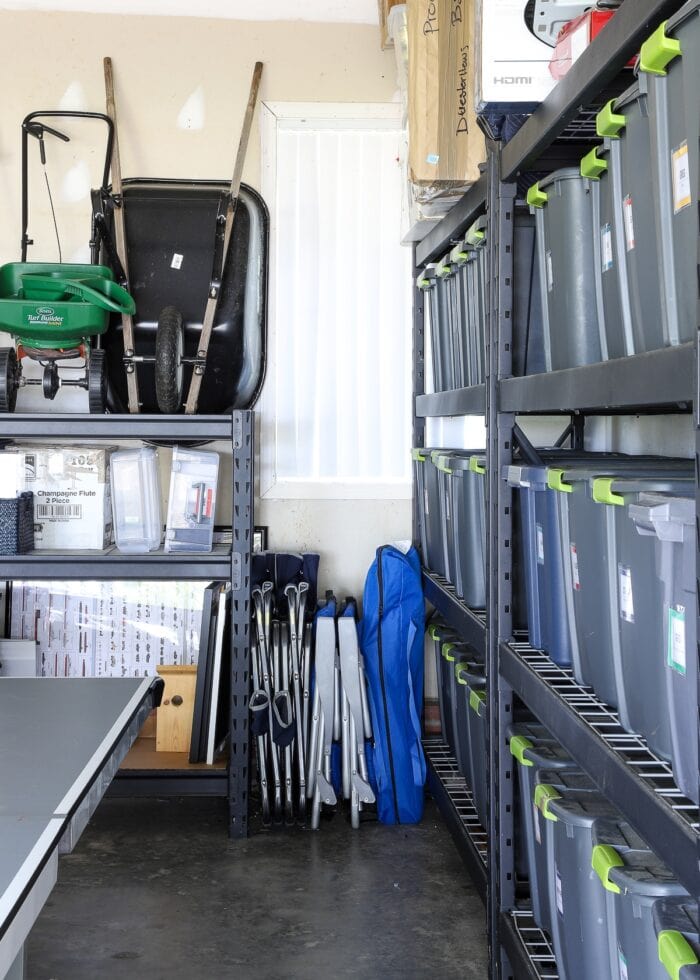 A corner shot of an organized garage, in which you can see storage bins, outdoor chairs, and lawn equipment