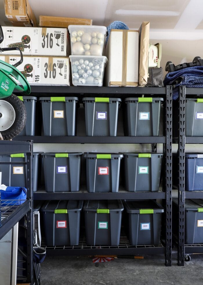 A set of garage storage shelves holding matching labeled totes with holiday decor bins on top.