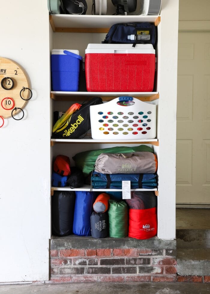 Built-in garage shelves holding camping equipment, coolers, and beach toys.