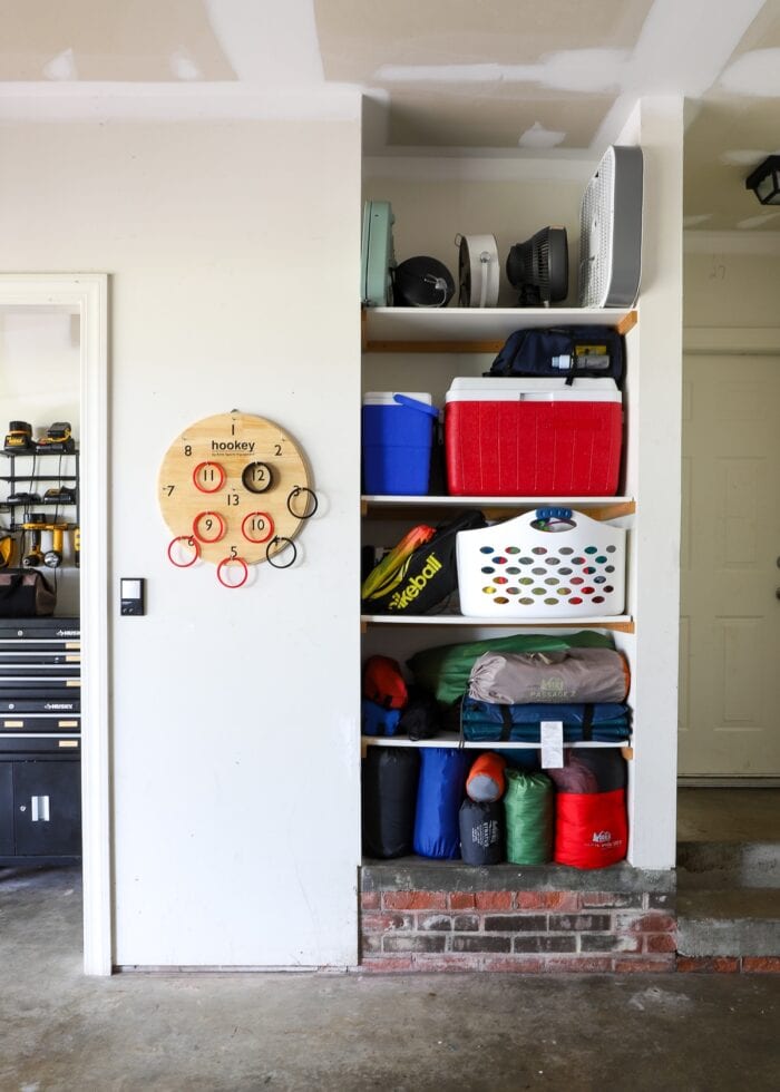 Built-in garage shelves holding camping equipment, coolers, and beach toys.
