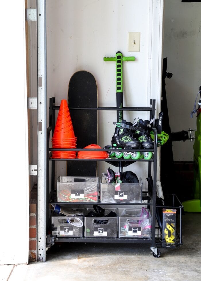 A rolling car inside a garage holding rollerblades, cones, skateboards, and other bins of toys.