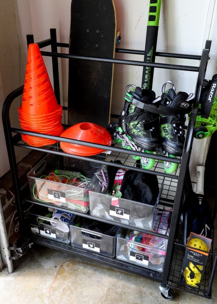 A rolling car inside a garage holding rollerblades, cones, skateboards, and other bins of toys.