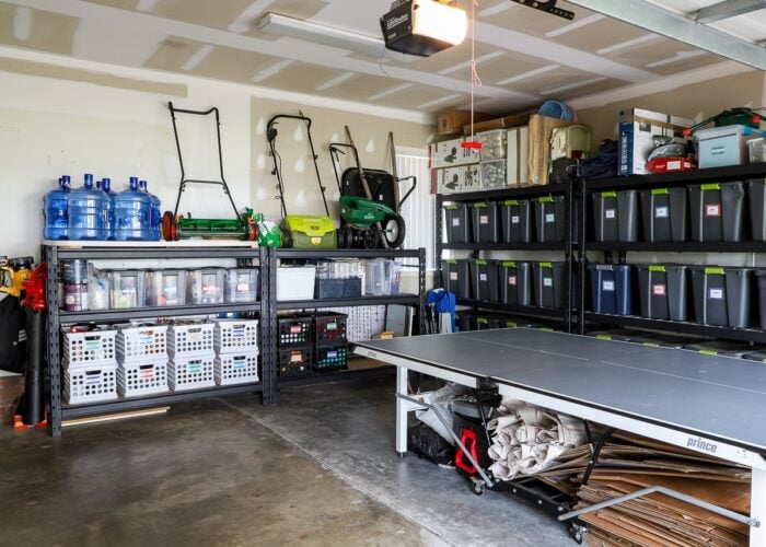 A wide shot of an organized garage feating tall storage shelves, lots of labeled bins, and a ping pong table.