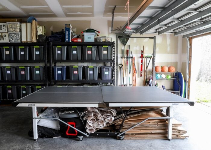 The side wall of an organized garage, showing a ping pong table, storage shelves, lawn equipment storage, and sports equipment strorage