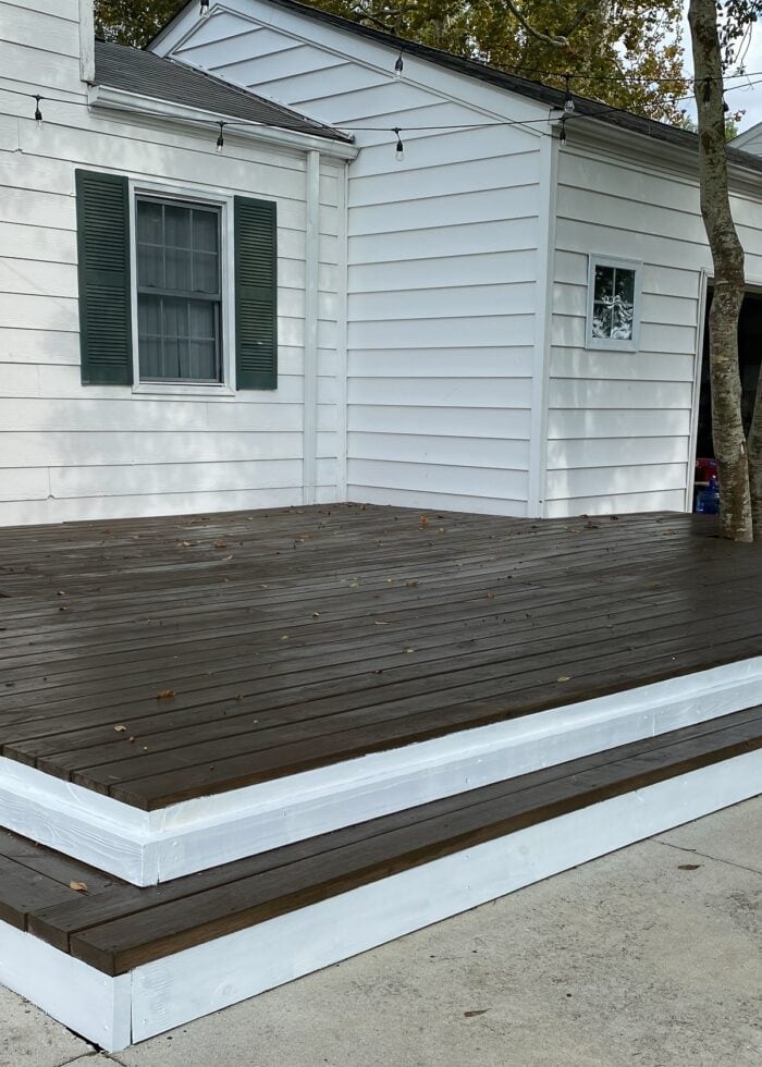 Wooden deck on the front of the house stained dark wood with white surround