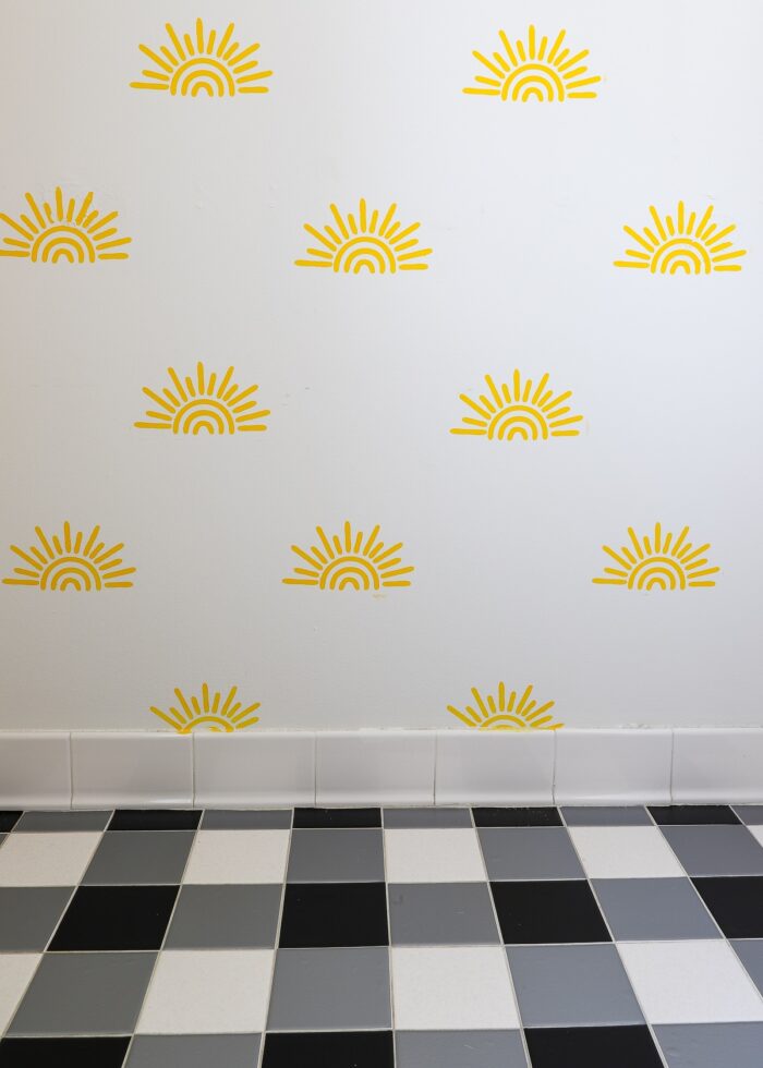 Yellow sunshine stenciled on a bathroom wall with black and white tile on the floor