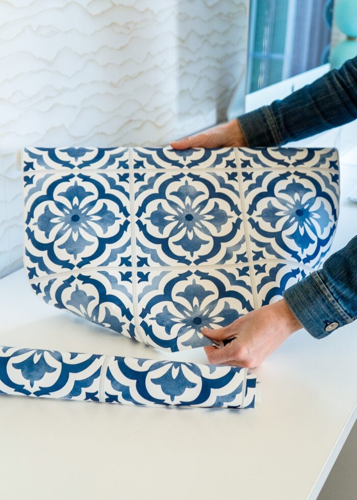 Megan unrolling a roll of blue and white tile backsplash wallpaper