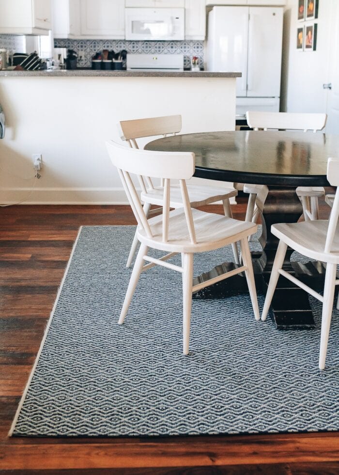 A wood dining table and chairs on top of a square outdoor rug