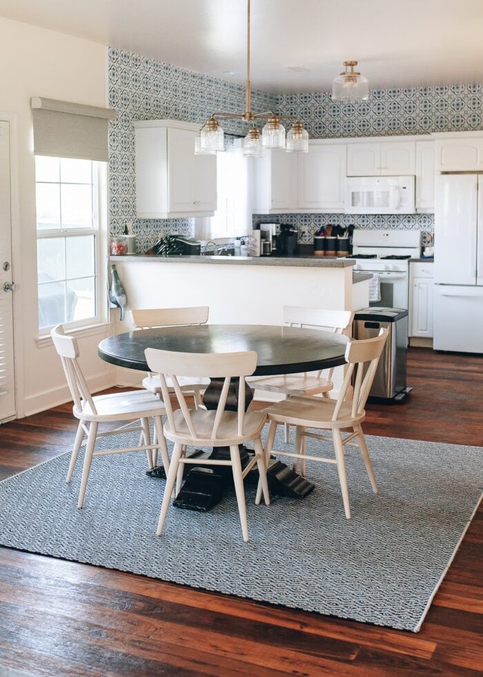 A wood dining table and chairs on top of a square outdoor rug