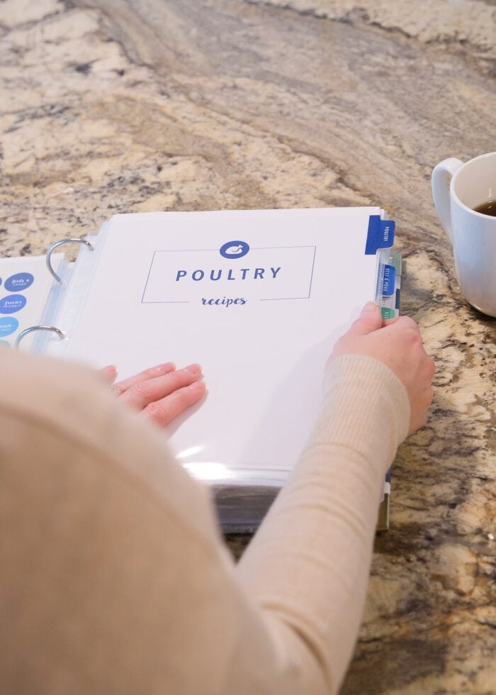 Megan's hands paging through a recipe binder opened to the Poultry section