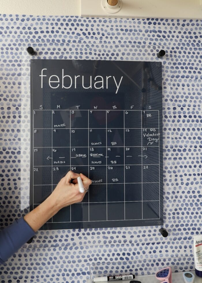Megan's hand writing on a dry-erase calendar with a white chalk marker