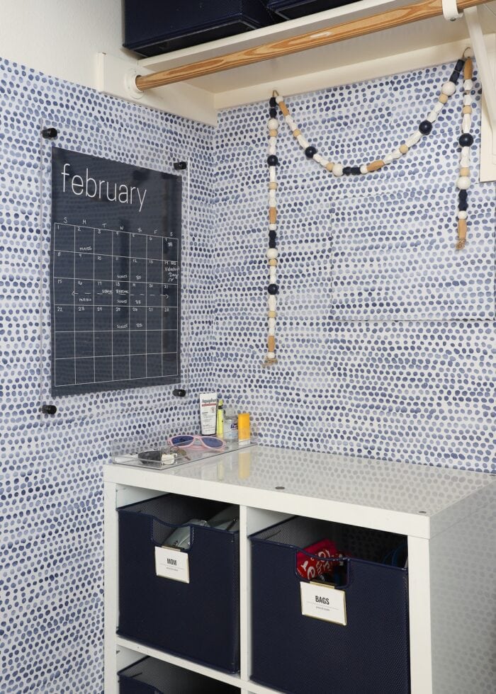 A cute mudroom counter setup on top of a cubby shelf featuring a wall calendar, bead garland and tray full of essentials