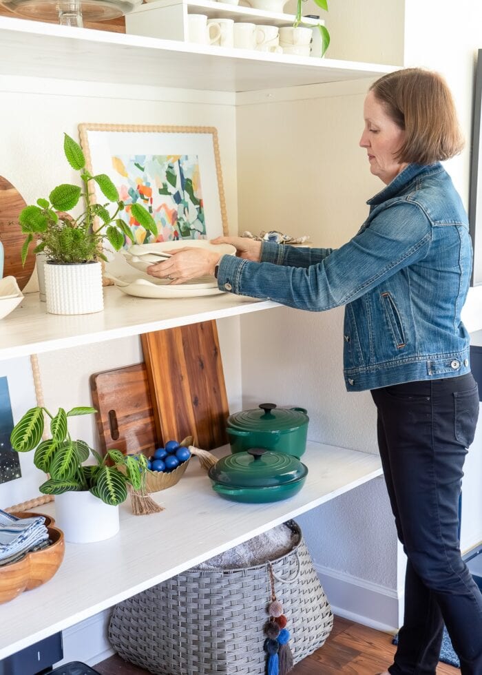 Megan putting down some serving platters on a set of floating shelves inside a wall nook