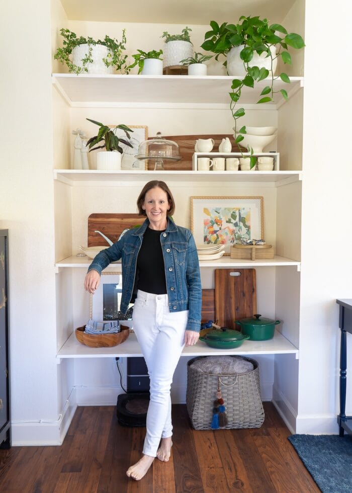 Megan from The Homes I Have Made standing in front of a wall nook filled with floating shelves, decorated with plants, dishes, and decorative items