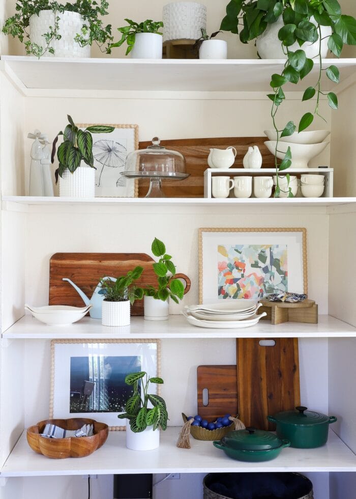 A floor-to-ceiling wall nook outfitted with basic wooden floating shelves that hold dishes, plants, artwork, and decor accessories.