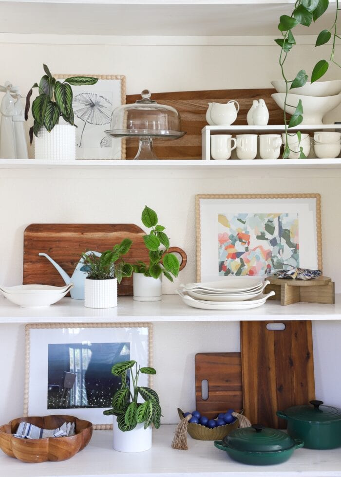 A floor-to-ceiling wall nook outfitted with basic wooden floating shelves that hold dishes, plants, artwork, and decor accessories.