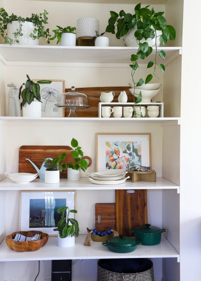 A floor-to-ceiling wall nook outfitted with basic wooden floating shelves that hold dishes, plants, artwork, and decor accessories.
