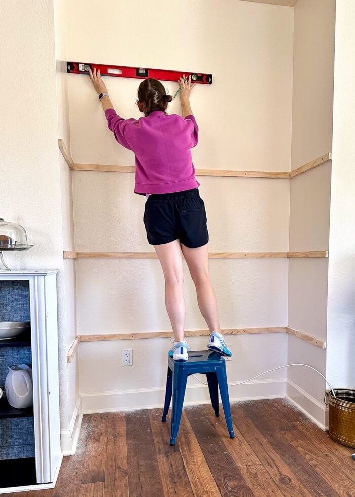 Megan measuring the height of a floating shelf inside an open wall nook using a level