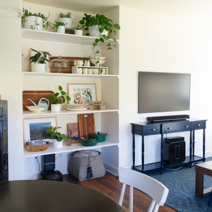 A floor-to-ceiling wall nook outfitted with basic wooden floating shelves that hold dishes, plants, artwork, and decor accessories.