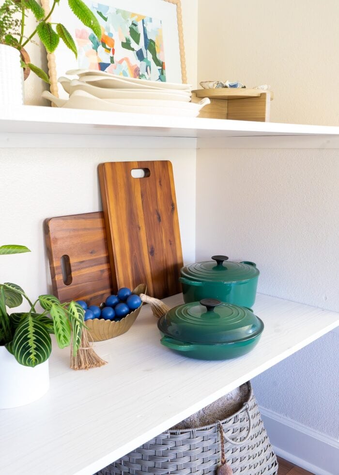 Wooden cutting boards, forest green pots and decorative objects on a wooden floating shelf inside a nook