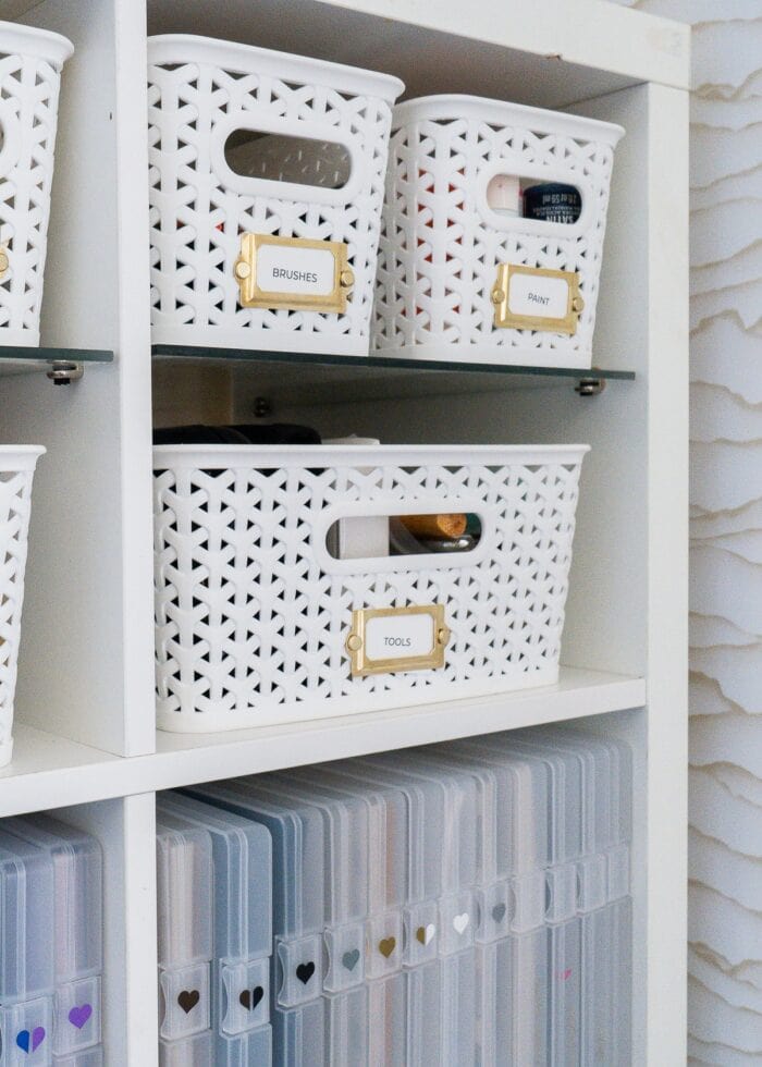 Two white baskets full of craft supplies on an IKEA Kallax shelf