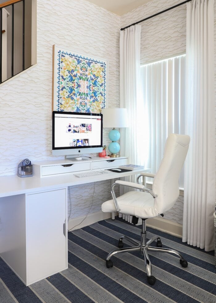 A computer on a white desk with colorful art hung above