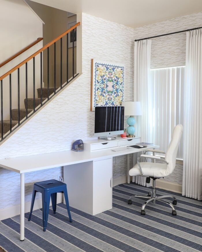 A computer on a white desk with colorful art hung above