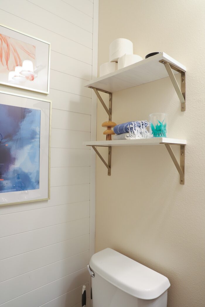 Simple floating shelves above a toilet decorated with white shiplap wall paneling