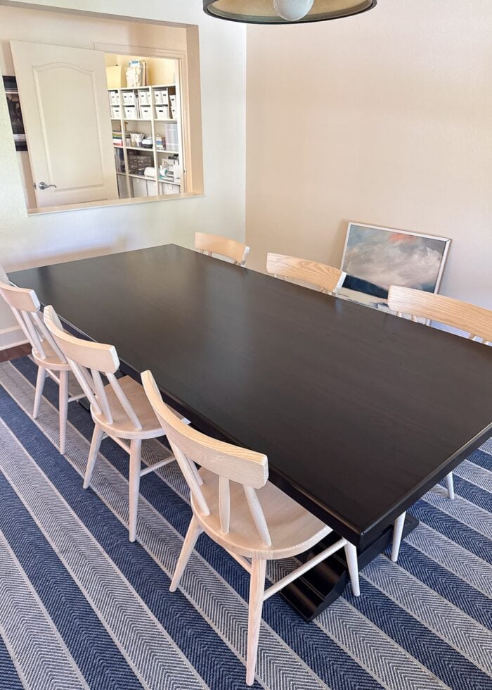 Dark dining room table with 6 light wood chairs on top of a blue striped rug