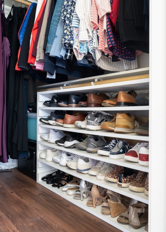 A shelf of shoes tucked underneath the lower hanging rod in a closet