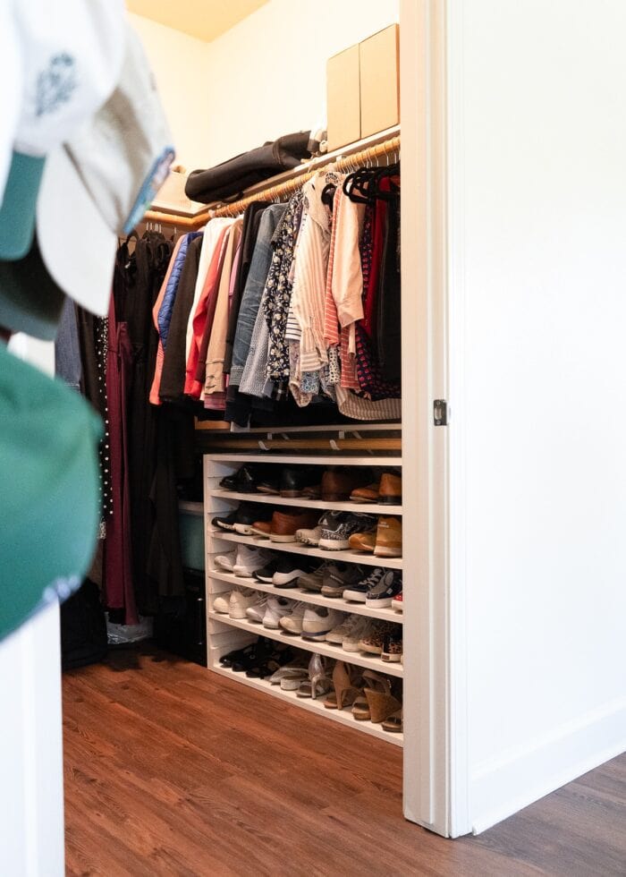 A walk-in closet with a shoe shelf sitting on the floor under the lower hanging rod